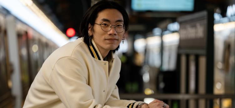 Young man standing outside NYC train at train station and smiling warmly at the camera