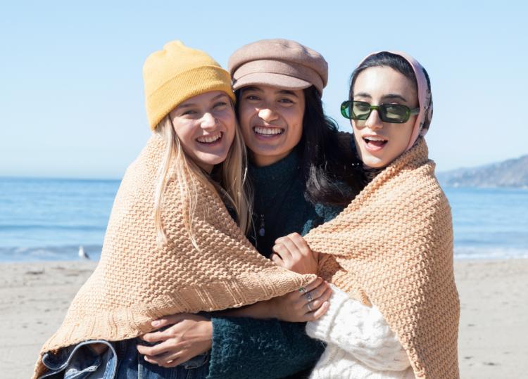 Gen Z friends smiling, wapped around a blanket together