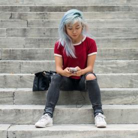 Young woman with colorful hair listening to music on headphones, sitting on steps