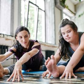 Low angle view of young woman with Down syndrome doing stretching exercises together with professional yoga instructor