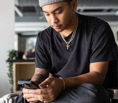 A young confident, filipino barber sits in his barber chair as he uses his cell phone.
